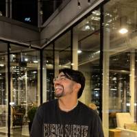 Photo of male student standing in front of windows with hands in pockets and laughing